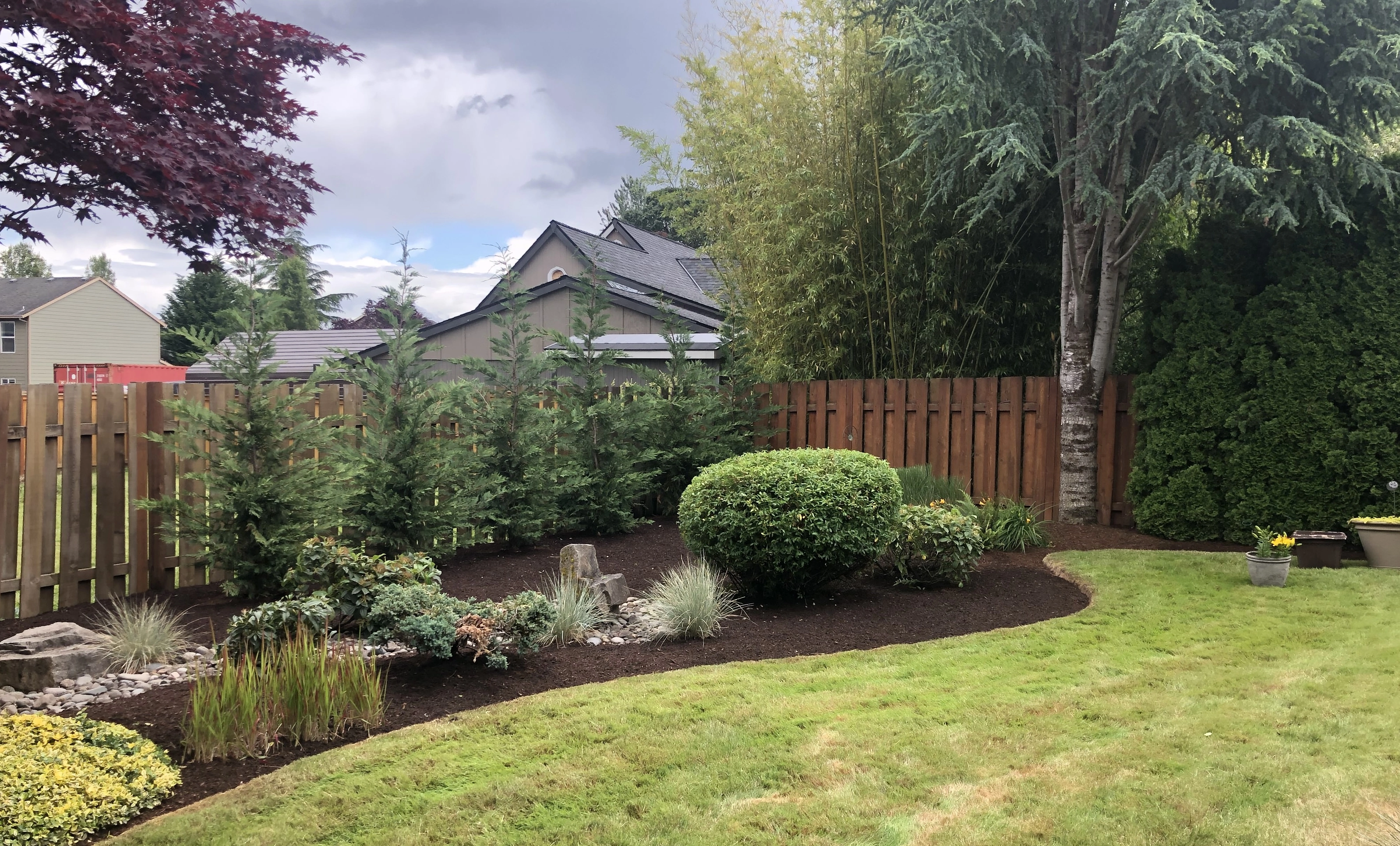 A backyard with a wooden fence, manicured lawn, and landscaped garden with shrubs and trees in Gresham, OR.